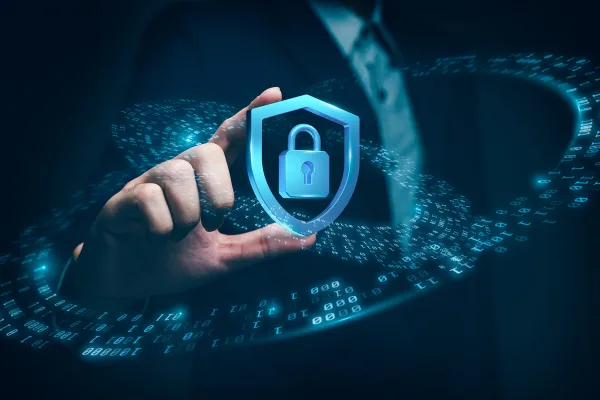 Hand holding a shield icon with a padlock in it to represent cybersecurity.