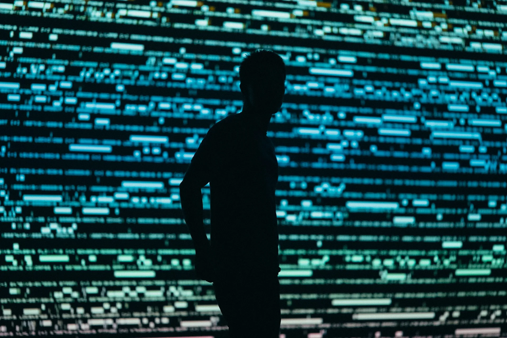 Silhouette of a man in front of a large screen with lines of code on it.